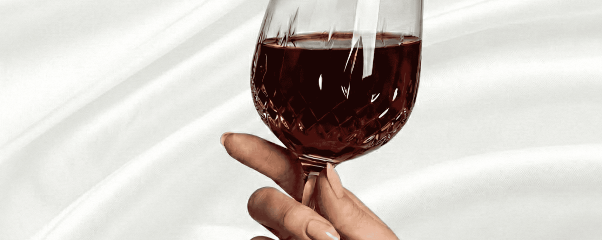 Manicured hand holding a textured wine glass with red liquid.